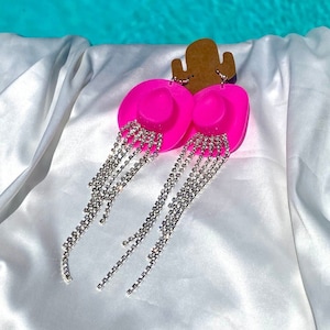 May include: A pair of pink cowboy hat shaped earrings with dangling rhinestone chains.