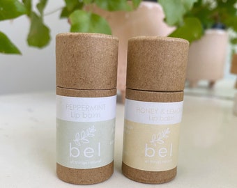 May include: Two brown cardboard tubes with white labels. The labels have a green leaf design and the text "bel all things natural". The left tube has the text "PEPPERMINT Lip balm" and the right tube has the text "HONEY & LEMON Lip balm".