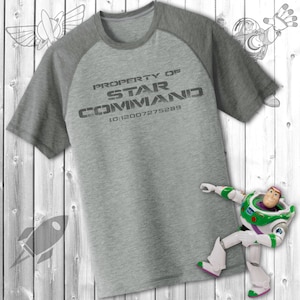 Op de afbeelding: Een grijs T-shirt met een zwart-witte afbeelding met de tekst "PROPERTY OF STAR COMMAND 10:12007275289".