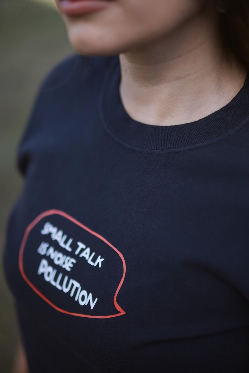 Puede incluir: Una camiseta negra con una burbuja de di&aacute;logo roja que dice "Small Talk is Noise Pollution".