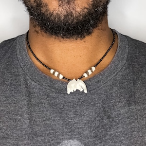 May include: A black beaded necklace with white and brown beads and a white bone pendant.