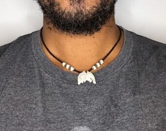 May include: A black beaded necklace with white and brown beads and a white bone pendant.