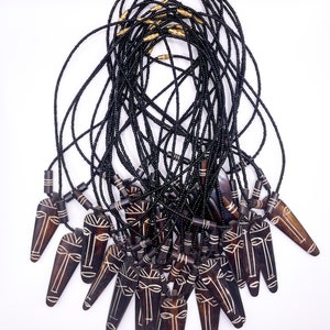 May include: A group of black beaded necklaces with wooden pendants featuring carved faces. The pendants are brown with white details and have a pointed shape.