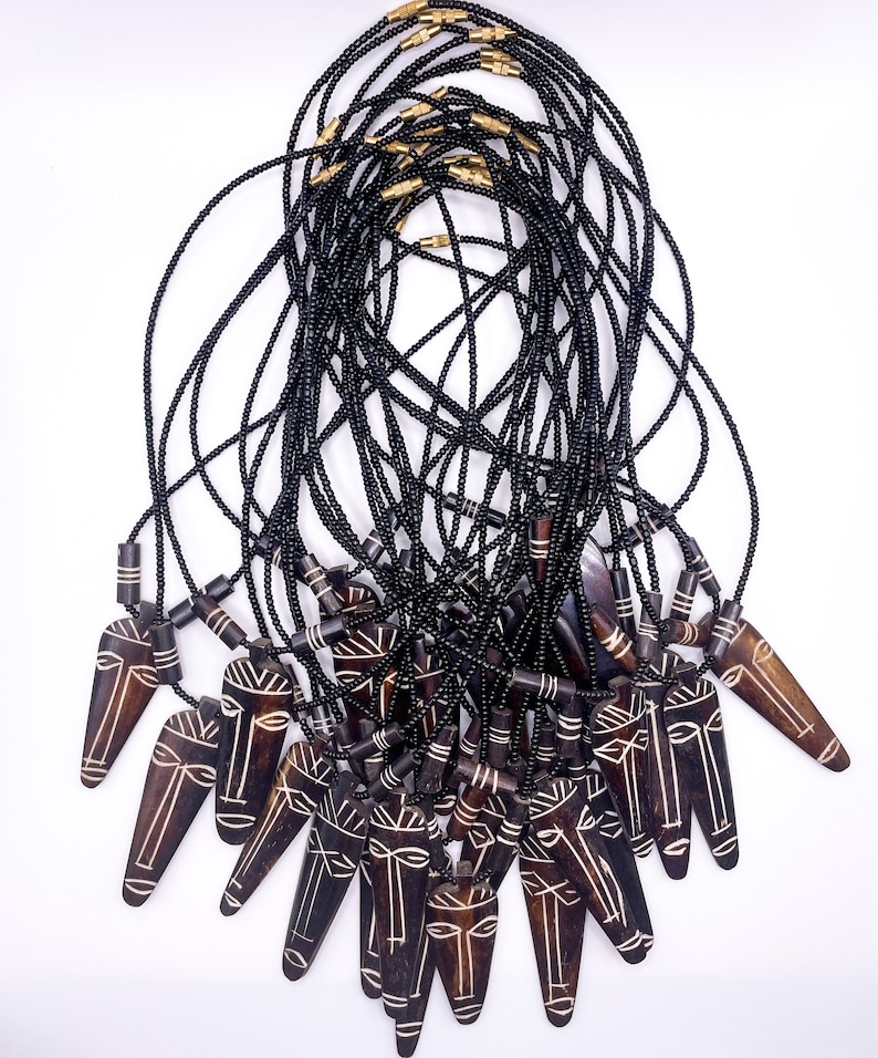May include: A group of black beaded necklaces with wooden pendants featuring carved faces. The pendants are brown with white details and have a pointed shape.
