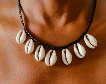May include: A black braided cord necklace with white cowrie shells hanging from it.