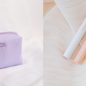 Puede incluir: Una bolsa de maquillaje de color lavanda con cremallera y el texto "Pretty Please" en la parte delantera. Dos pequeños tubos de maquillaje, uno blanco y otro melocotón, están sobre una tela blanca y melocotón.