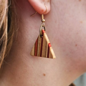 May include: Triangle-shaped earrings made from wood with red and brown stripes. The earrings are attached to gold hooks.