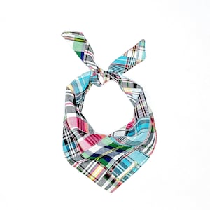 May include: A blue, pink, and green plaid bandana with a white border. The bandana is tied in a knot at the top and has a small, gold tag with the word "Handmade" on it.