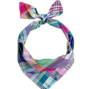 May include: A triangular pet bandana featuring a multi-coloured plaid pattern in shades of pink, teal, green, blue, and white. The fabric accessory is tied at the top with a knot, creating a pointed shape at the bottom with visible stitched edges.
