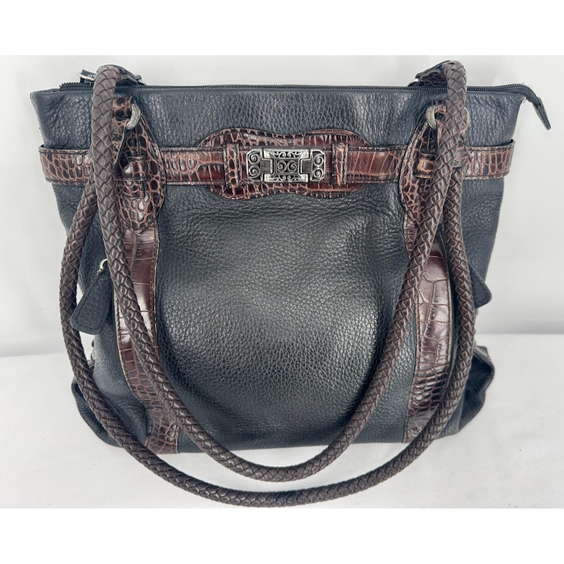 May include: Black leather tote bag with brown crocodile-embossed accents and braided handles. The bag features a silver-tone buckle closure and a textured leather exterior. A stylish and functional handbag.