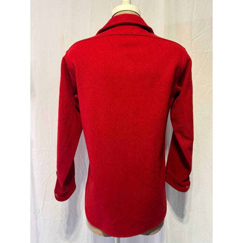 May include: A bright red blazer with long sleeves and a collared neckline. The back view of the blazer shows a tailored fit and button details on the sleeves. The blazer is displayed on a mannequin against a white backdrop.