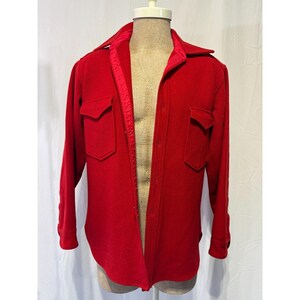 May include: A bright red wool shirt jacket with two chest pockets and a collared neckline. The jacket is buttoned down the front and has long sleeves with buttoned cuffs. The interior collar lining is a contrasting red.