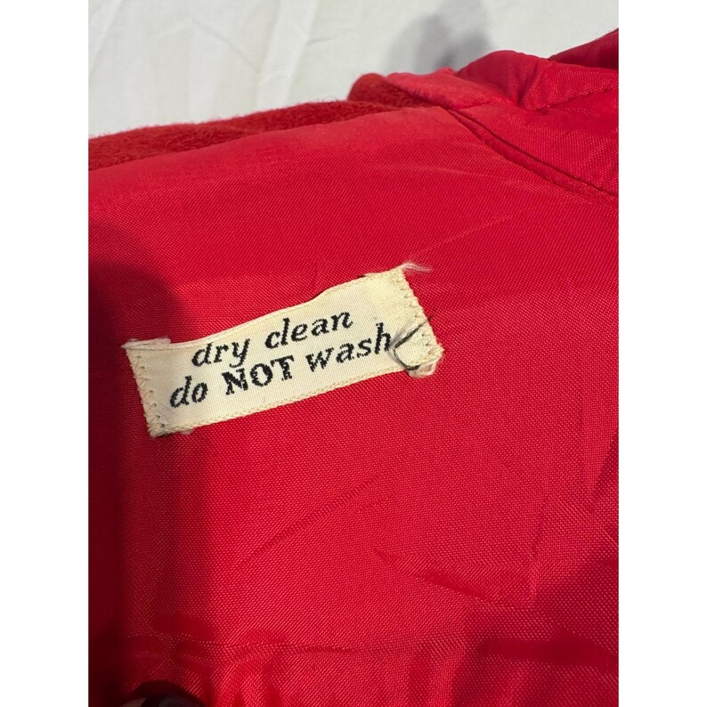 May include: Close-up of a bright red garment with a tag that reads "dry clean do NOT wash". The fabric appears to be a smooth, possibly satin-like material. The tag is white with black text.