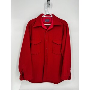 May include: A bright red wool shirt with two chest pockets and a button-down front. The shirt has a collar and long sleeves with buttoned cuffs. The shirt is hanging on a white hanger against a white background.