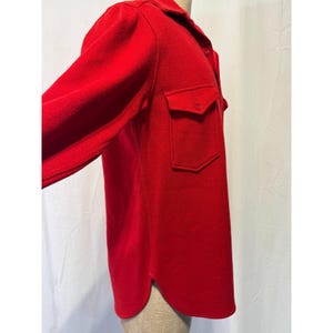 May include: A bright red long-sleeved shirt with two chest pockets and a collared neckline. The shirt is made of a textured fabric and has a button-down front. The sleeves are long and the shirt has a curved hemline.
