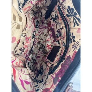 May include: Open view of a dark blue handbag interior. The inside features a floral pattern in pink, purple, and black on a beige background. A zippered pocket and several open pockets are visible.