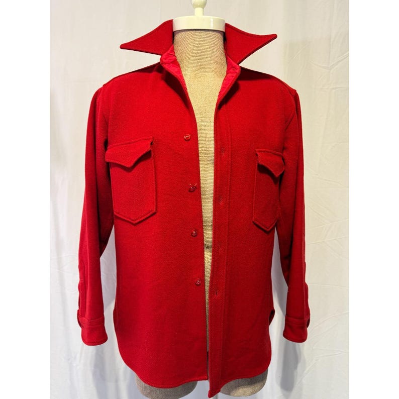 May include: A vibrant red wool shirt jacket with two front pockets and a wide collar. The jacket has long sleeves with buttoned cuffs and a button-up front. The jacket is displayed on a mannequin.