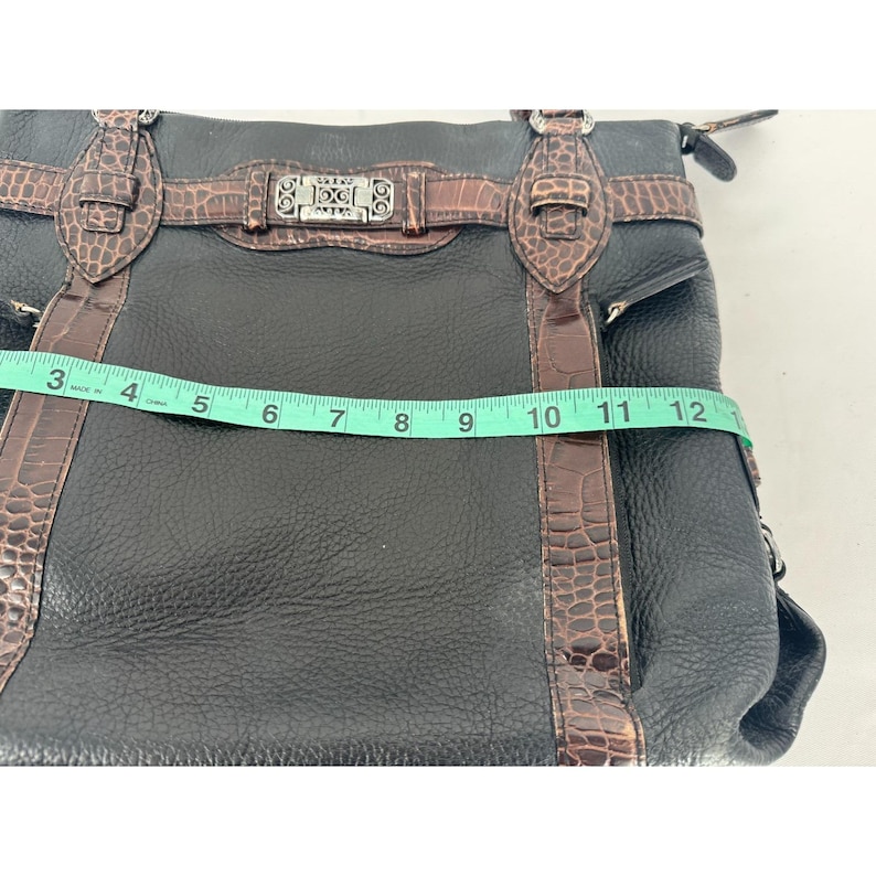 May include: Black leather handbag with brown crocodile-textured accents. The bag features a silver-tone buckle and hardware. The measurement across the top is approximately 12 inches.
