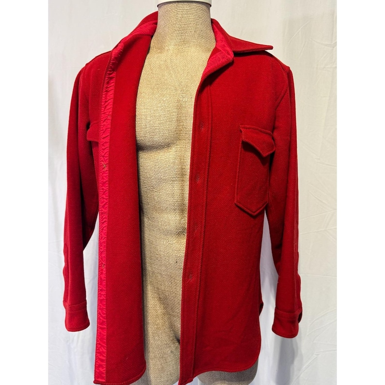 May include: A vibrant red wool shirt jacket with a collared neckline and button-down closure. Features a single chest pocket and a satin lining along the open front. The long sleeves have buttoned cuffs.