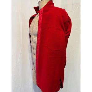 May include: A vibrant red jacket with a classic design, featuring a collared neckline and a single pocket. The jacket is displayed on a mannequin, showcasing its tailored fit and the rich color of the fabric. A contrasting red trim runs down the front.