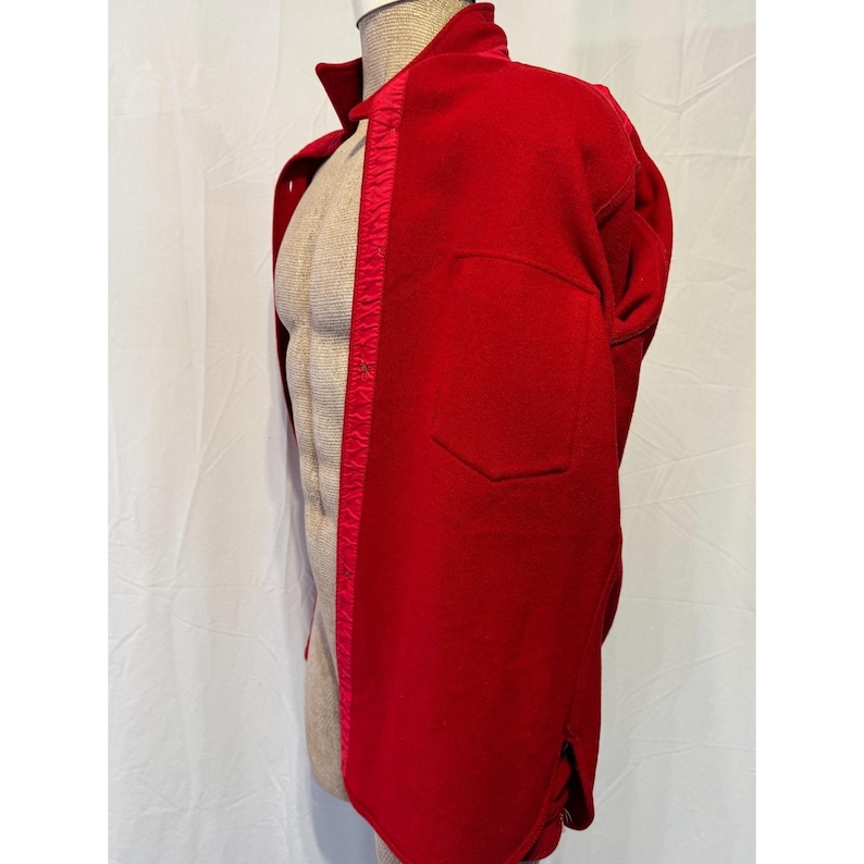 May include: A vibrant red jacket with a classic design, featuring a collared neckline and a single pocket. The jacket is displayed on a mannequin, showcasing its tailored fit and the rich color of the fabric. A contrasting red trim runs down the front.