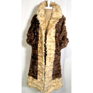 May include: A long, vintage faux fur coat in shades of brown and beige. The coat features a wide collar and vertical stripes of varying colours. The coat is displayed on a white hanger against a white background, showcasing its full length and design.