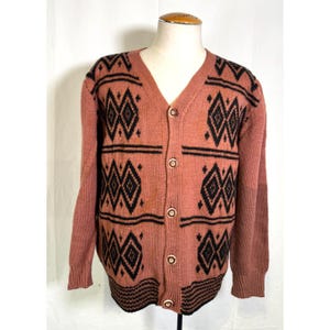 Könnte beinhalten: Knopf-Cardigan in einem gedämpften rötlich-braunen Farbton, verziert mit einem geometrischen schwarzen Rautenmuster. Der Pullover hat einen V-Ausschnitt und lange Ärmel mit geripptem Saum und Bündchen. Das Design wiederholt sich.