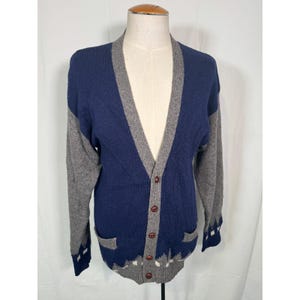 Könnte beinhalten: Ein blauer und grauer Strickcardigan mit V-Ausschnitt und Knopfleiste. Der Cardigan hat ein geometrisches Muster an den Ärmeln und am Saum.