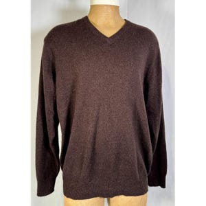 Pode incluir: Um suéter marrom com decote em V e mangas compridas. O suéter é feito de um material macio e é exibido em um manequim. A cor é um marrom profundo e rico.