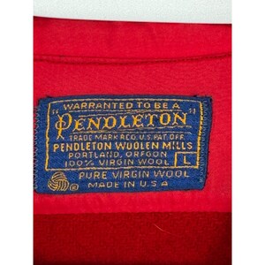 May include: Close-up of a red garment with a blue label. The label reads "PENDLETON" and "100% VIRGIN WOOL" with the size "L". The label also states "MADE IN U.S.A."