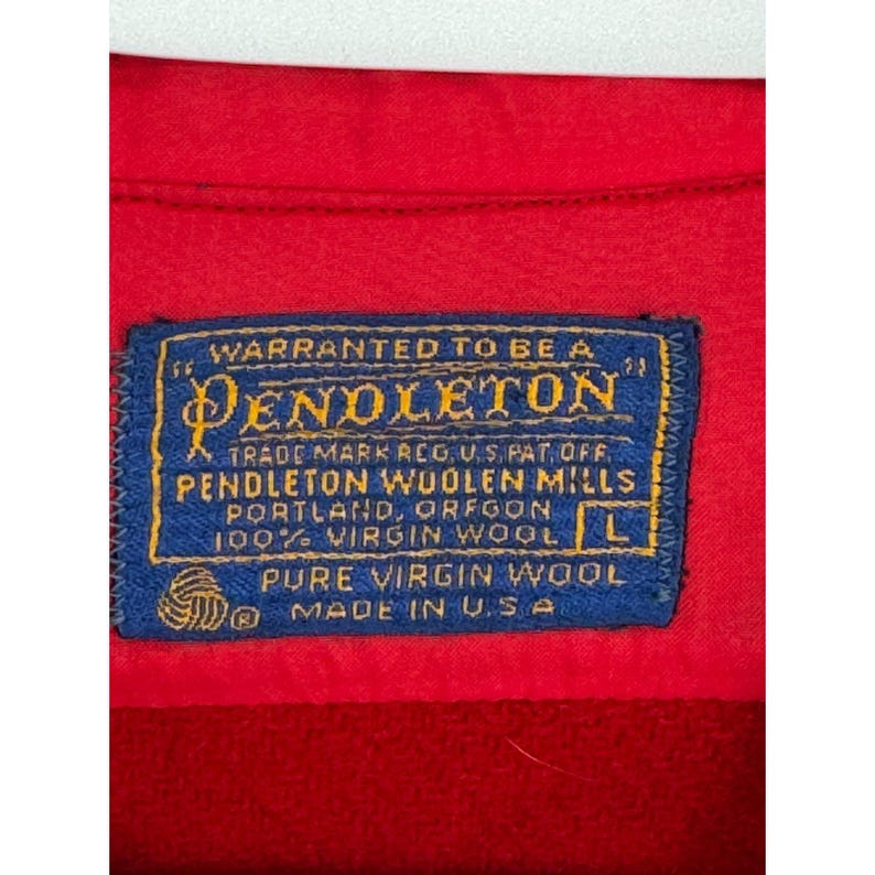 May include: Close-up of a red garment with a blue label. The label reads "PENDLETON" and "100% VIRGIN WOOL" with the size "L". The label also states "MADE IN U.S.A."