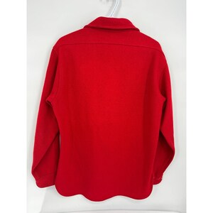 May include: A solid red long-sleeve shirt with a collared neckline. The shirt is made of a thick material and has buttoned cuffs. The shirt is hanging on a white hanger against a white background.