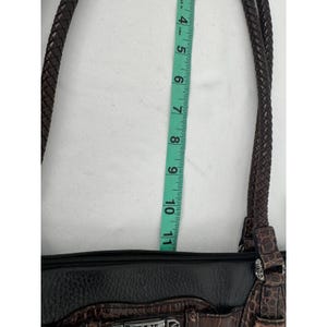 May include: A brown and black handbag with braided straps. The bag has a black zipper and a decorative silver clasp. The measurement from the top of the bag to the bottom is approximately 10 inches.