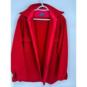 May include: A bright red jacket with a wide collar and two front pockets. The jacket is hanging on a white hanger. The interior lining is a lighter shade of red. A small label is visible inside the collar.