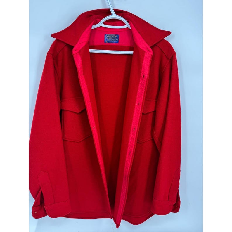 May include: A bright red jacket with a wide collar and two front pockets. The jacket is hanging on a white hanger. The interior lining is a lighter shade of red. A small label is visible inside the collar.