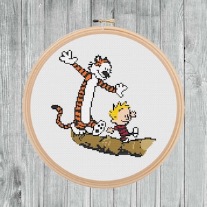 May include: A cross-stitch pattern of Calvin and Hobbes, a young boy and his tiger, standing on a log. Calvin is wearing a red shirt and blue trousers, and Hobbes is wearing orange and black stripes.