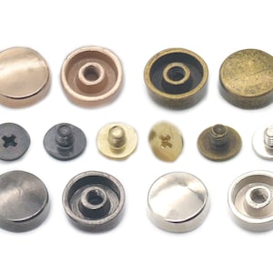 May include: Assortment of metal rivets in various finishes, including gold, silver, brass, and black. The rivets have a domed head and a threaded shank for attaching to fabric or leather.