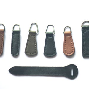 May include: Assortment of seven leather zipper pulls in various colors, including brown, black, and green. The zipper pulls are all about 2 inches long and have a metal ring at the top.