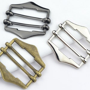 May include: Three metal belt buckle sliders in different finishes: black, silver, and antique gold. Each slider has three bars for adjusting the belt length.