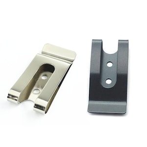 Puede incluir: Dos clips de cintur&oacute;n de metal, uno plateado y otro negro. Ambos clips tienen una abertura en forma de U y tres peque&ntilde;os agujeros.