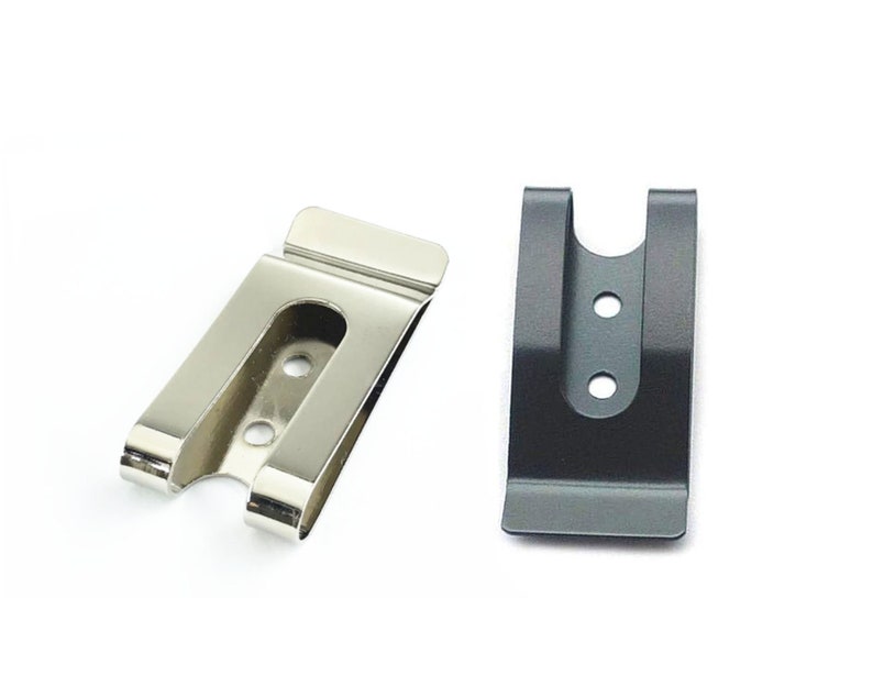 Puede incluir: Dos clips de cintur&oacute;n de metal, uno plateado y otro negro. Ambos clips tienen una abertura en forma de U y tres peque&ntilde;os agujeros.