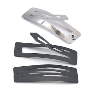 May include: Three hair clips, two black and one silver. The black clips are slightly curved and have a rectangular shape with a small hole at one end. The silver clip is also curved and has a rectangular shape with a small hole at one end. The silver clip has a small, decorative piece at the top.