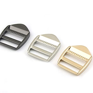 Peut inclure: Trois boucles coulissantes en métal dans différentes finitions : noir, argent et or. Chaque boucle a deux fentes et une surface texturée.