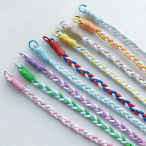 May include: Braided cord straps in various colors, including pink, green, purple, blue, red, yellow, orange, and tan. Each strap has a metal loop at the end. The cords are made of a soft material and are suitable for crafting or accessories.