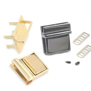 Pode incluir: Um conjunto de fechos para malas de metal dourado e preto com dois conjuntos de laços de metal e dois pequenos parafusos.