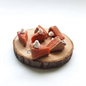 Könnte beinhalten: Sechs Miniatur-Kürbiskuchenstücke mit weißem Frosting auf einer Holzscheibe. Die Kuchen sind aus Polymer Clay gefertigt und haben ein realistisches Aussehen.