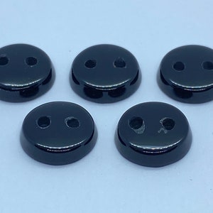 May include: Five black plastic buttons with two holes each. The buttons are round and have a glossy finish.