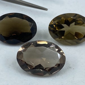 May include: Three oval-shaped smoky quartz gemstones with faceted edges. The gemstones are a light brown colour and have a translucent appearance.