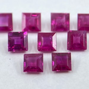 Może przedstawiać: Dziesięć kwadratowych rubinów, każdy o głębokim różowym odcieniu, ułożonych jest w przesunięty wzór na białym tle.