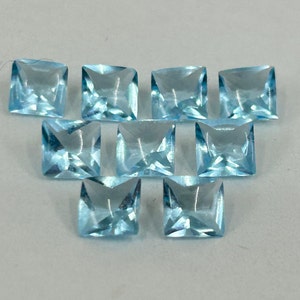 May include: Ten square-shaped, light blue gemstones. The gemstones are faceted and have a clear, glassy appearance.